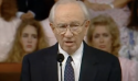 President Hinckley speaking from a pulpit with a choir behind him.