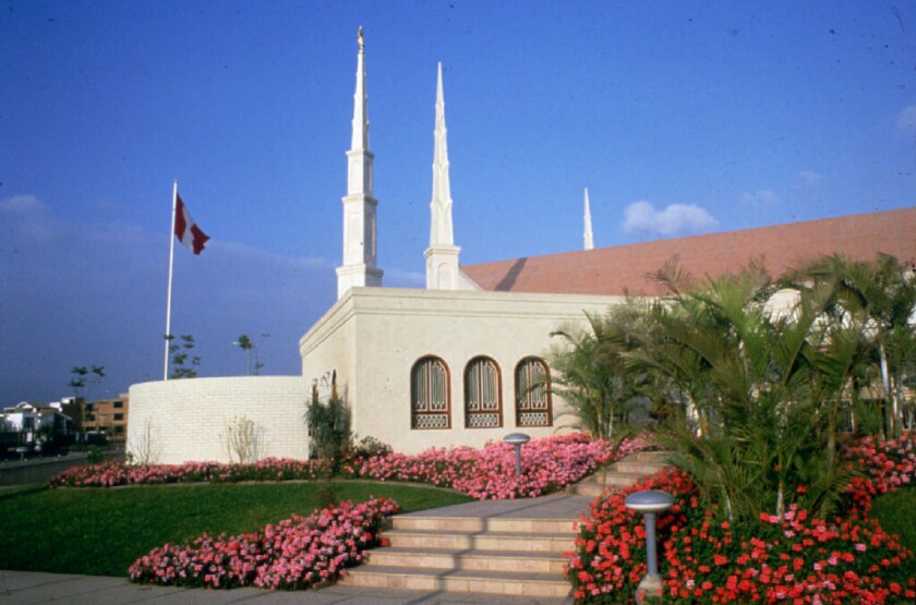 A side view of the Lima Peru Temple, a building with a red peaked roof on top.