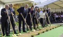 A line of people in Sunday best shoveling dirt with golden shovels.