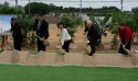 Three men in suits and and two women in church dress holding ceremonial golden shovels and digging into the ground.