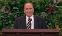 A man in a black suit stands behind a pulpit and smiles.