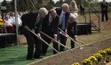 A row of people in formal clothing shovel dirt with golden shovels.