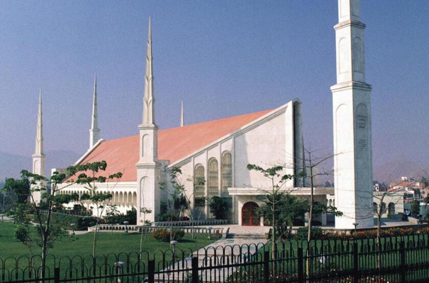 The Lima Peru Temple, a white building with a peaked roof on top, with blue skies above.