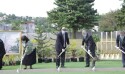 A line of people in formal clothing holding silver shovels.